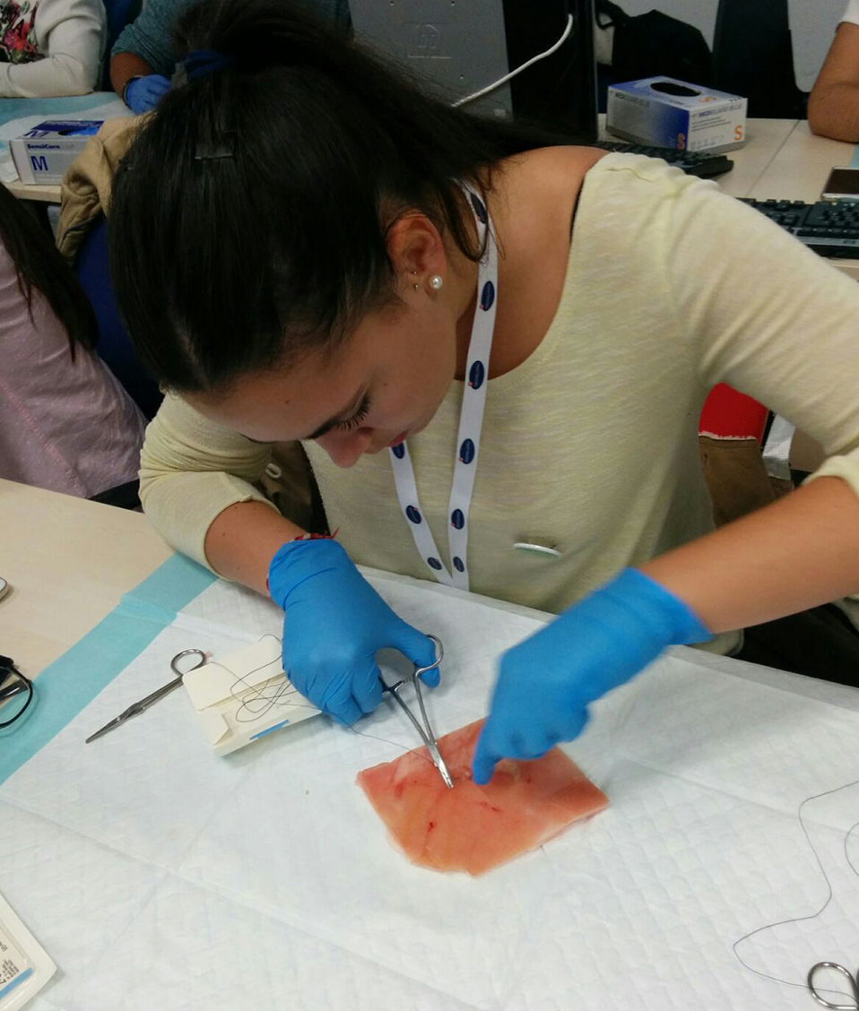 Estudiante con guantes realizando unas prácticas cosiendo unos puntos de sutura sobre un trozo de piel artificial