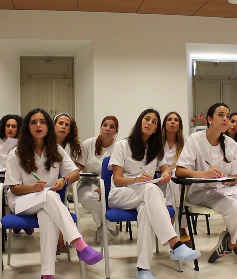 Estudiantes de enfermería en aula con sillas con pala atendiendo a una clase